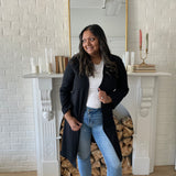 woman wearing a black long duster cardigan and a white crewneck t-shirt with jeans and white sneakers. Standing in front of a mirror and fireplace