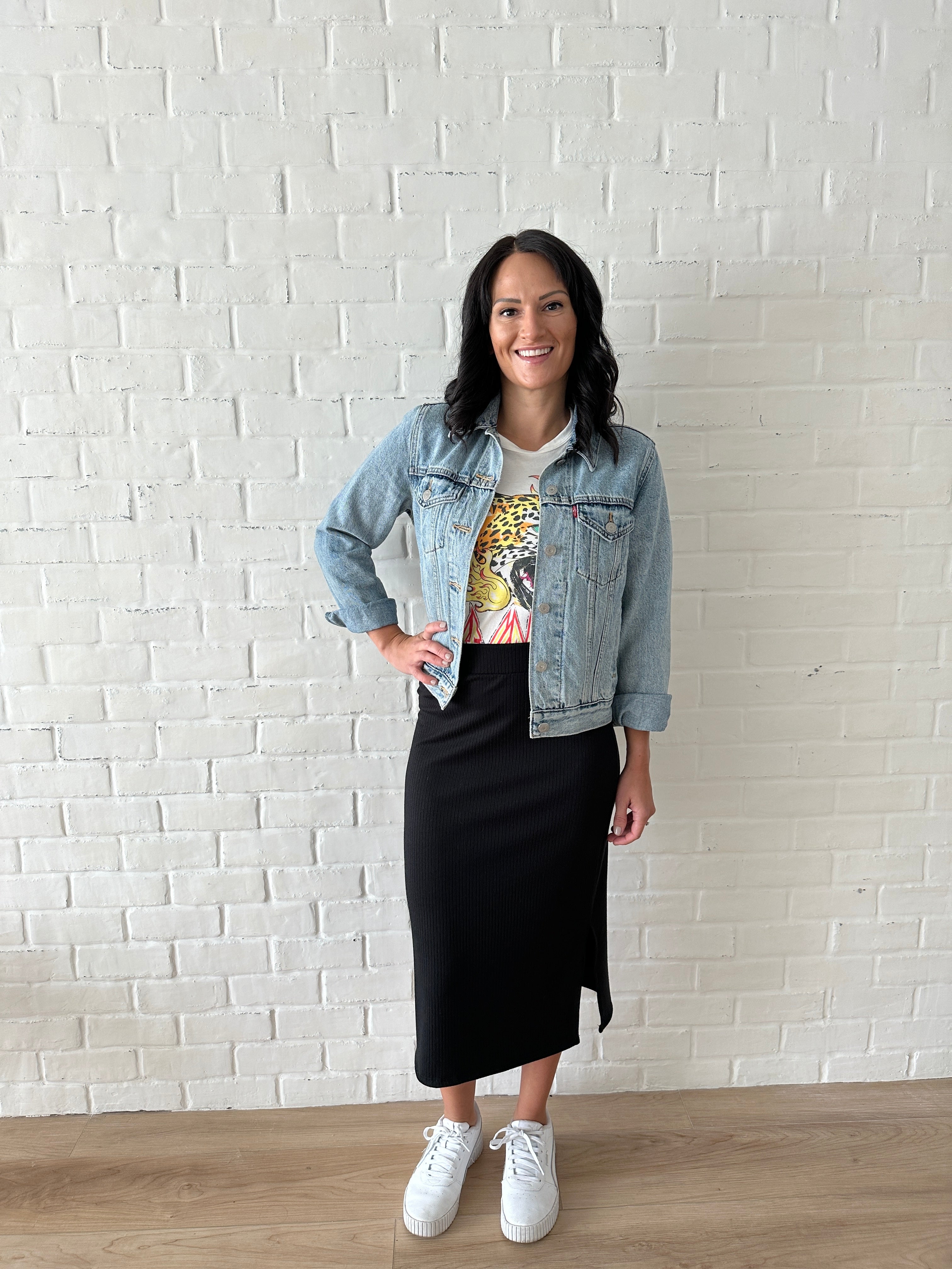 woman wearing jean jacket, graphic tee and black ribbed midi skirt with white sneakers