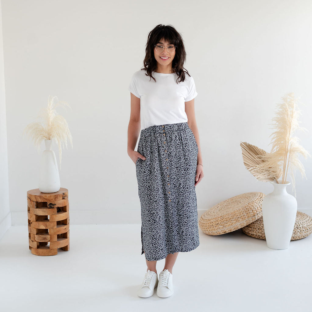 Woman wearing a white t-shirt and patterned skirt standing in a minimalistic room. Apparel made in Canada