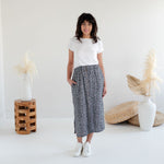 Woman wearing a white t-shirt and patterned skirt standing in a minimalistic room. Apparel made in Canada