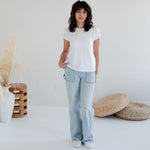 Woman wearing a white t-shirt and light blue jeans standing in a minimalistic room with woven items. Apparel made in Canada