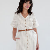 Woman wearing a white dress with buttons and a brown belt on a plain background