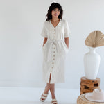 Woman wearing a white dress with black stripes in a minimalistic setting.