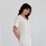 Woman wearing a white ribbed dress with buttons on a plain background