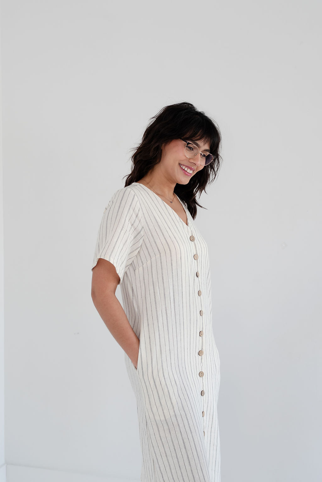 Woman wearing a white ribbed dress with buttons on a plain background