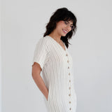Woman wearing a white ribbed dress with buttons on a plain background