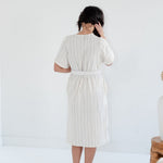 Woman wearing a white dress with vertical stripes against a plain background