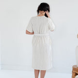 Woman wearing a white dress with vertical stripes against a plain background