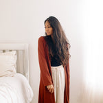Woman standing in a bedroom with a long red brown cardigan and loungewear
