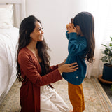 woman wearing a long cardigan and loungewear sitting on the floor with a young girl who is holding a camera