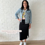 woman wearing jean jacket, graphic tee and black ribbed midi skirt with white sneakers