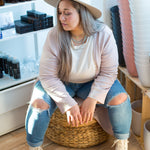 woman sitting wearing a long pink cardigan, cream sweater and jeans