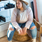 woman sitting wearing a long pink cardigan, cream sweater and jeans