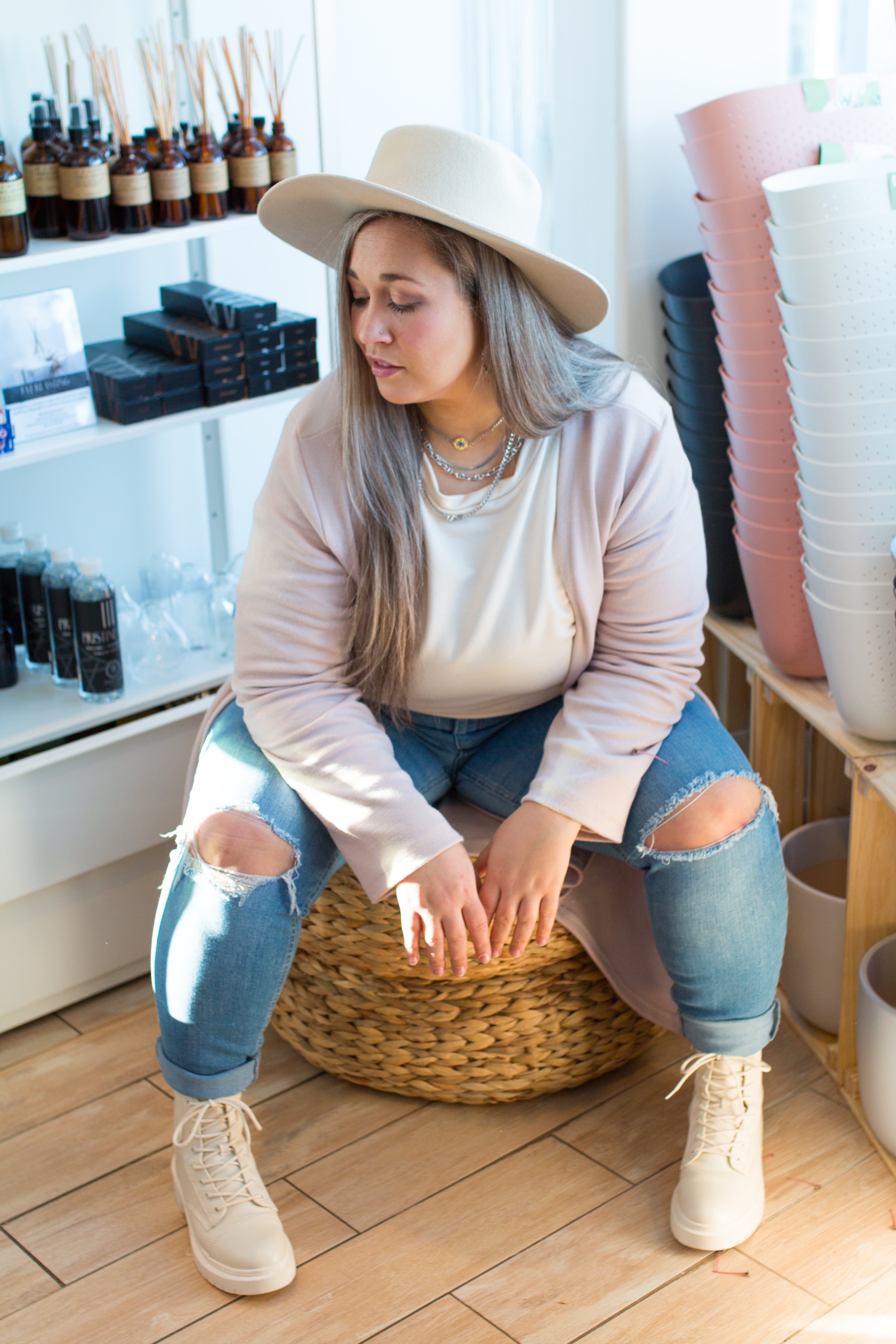 woman sitting wearing a long pink cardigan, cream sweater and jeans