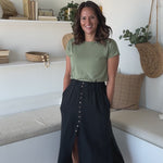 woman standing and twirling wearing a sage green t-shirt and a black button up midi skirt