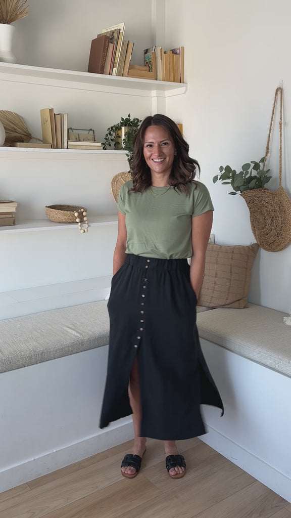 woman standing and twirling wearing a sage green t-shirt and a black button up midi skirt