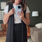 Woman taking a mirror selfie in a living room wearing a black vest and black midi skirt. Made in Canada video.