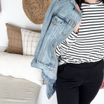 woman wearing black and white bamboo sweatshirt with denim jacket drapped over her shoulder. standing wearing black bamboo tapered joggers with white sneakers