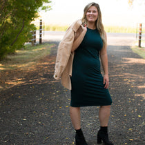 blonde woman wearing dark green tank dress holding a shacket over her shoulder standing on a road