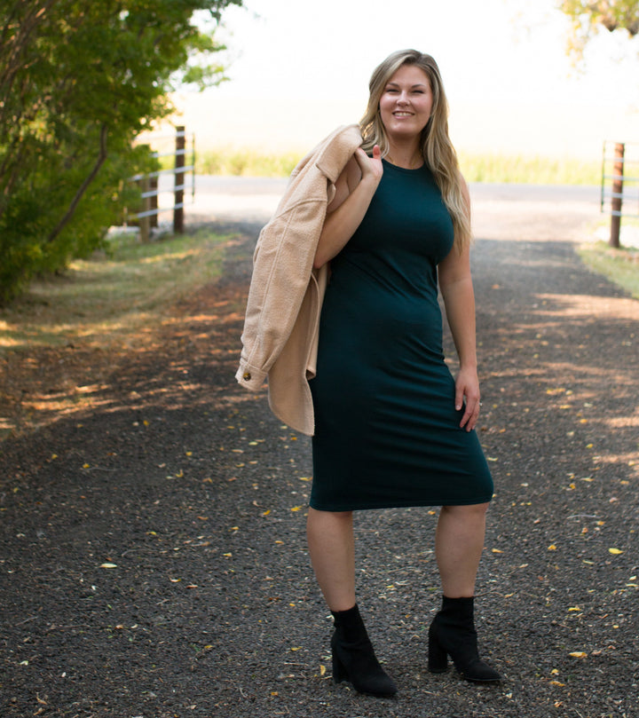 blonde woman wearing dark green tank dress holding a shacket over her shoulder standing on a road