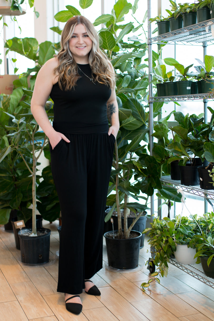 woman wearing a black tank top and black wide leg pants in front of plants