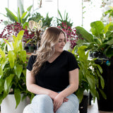 blonde woman sitting in plants with black v neck t shirt