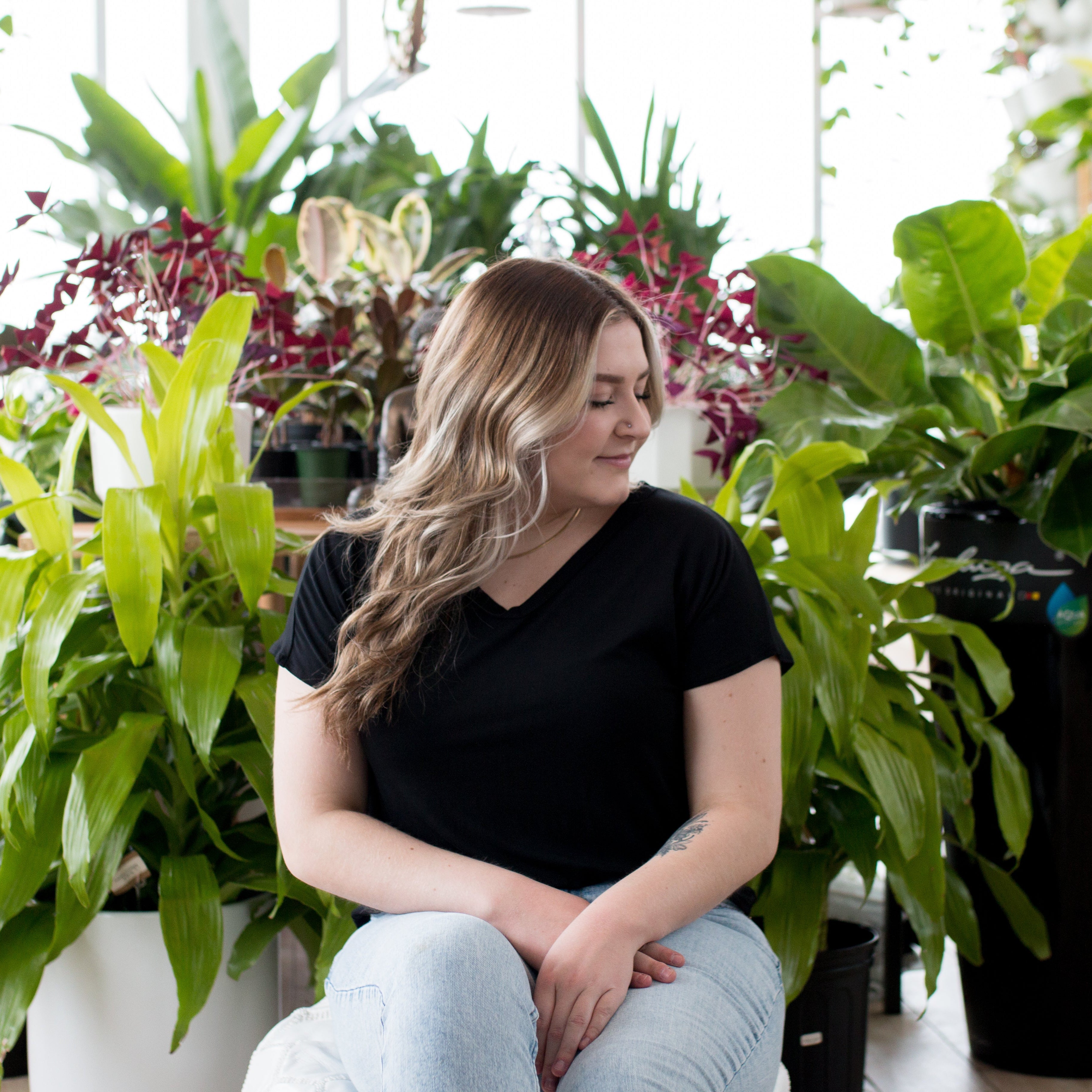 blonde woman sitting in plants with black v neck t shirt