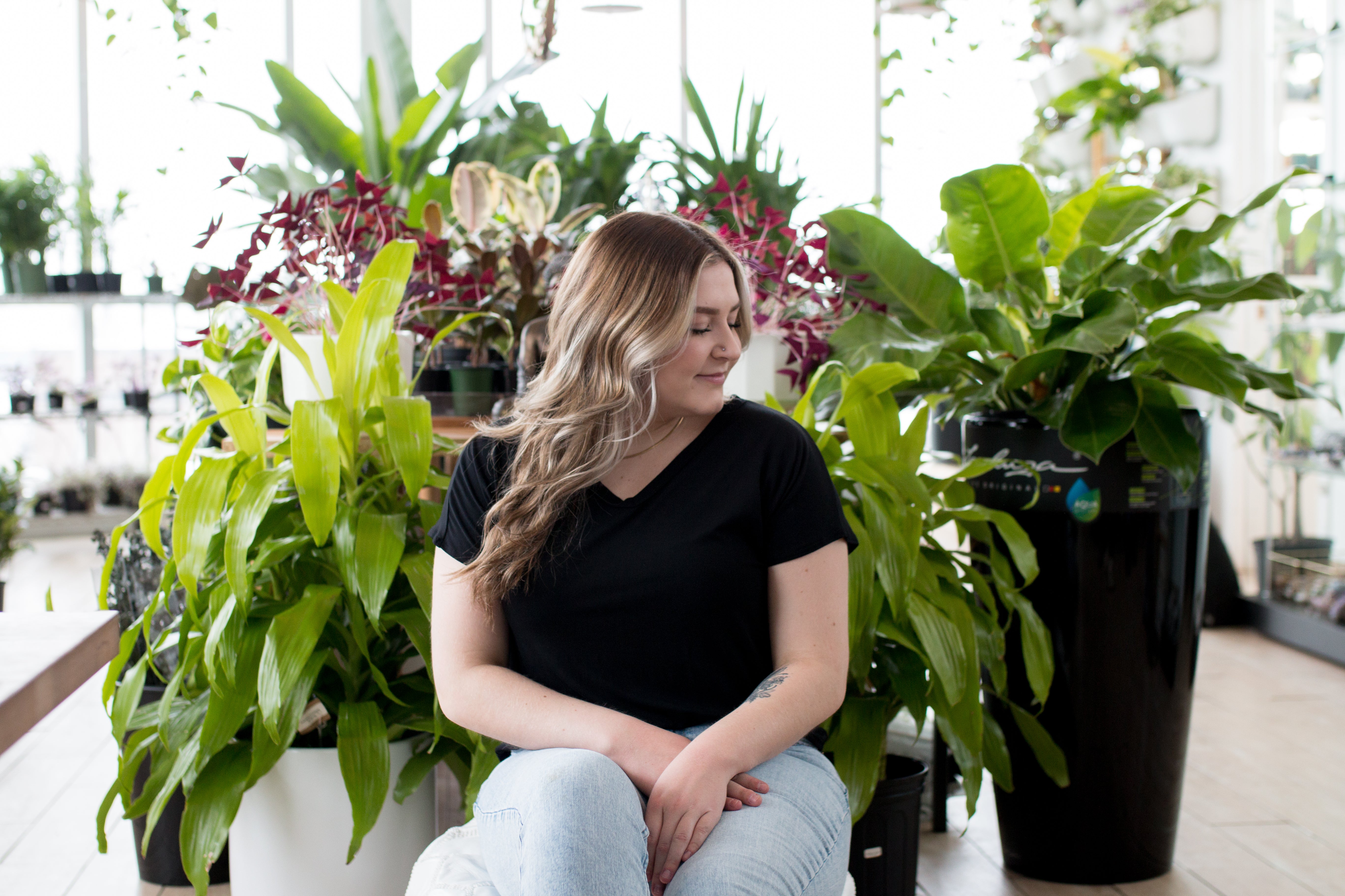 blonde woman sitting in plants with black v neck t shirt
