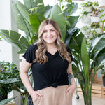 blonde woman standing in black vneck t shirt in front of plant
