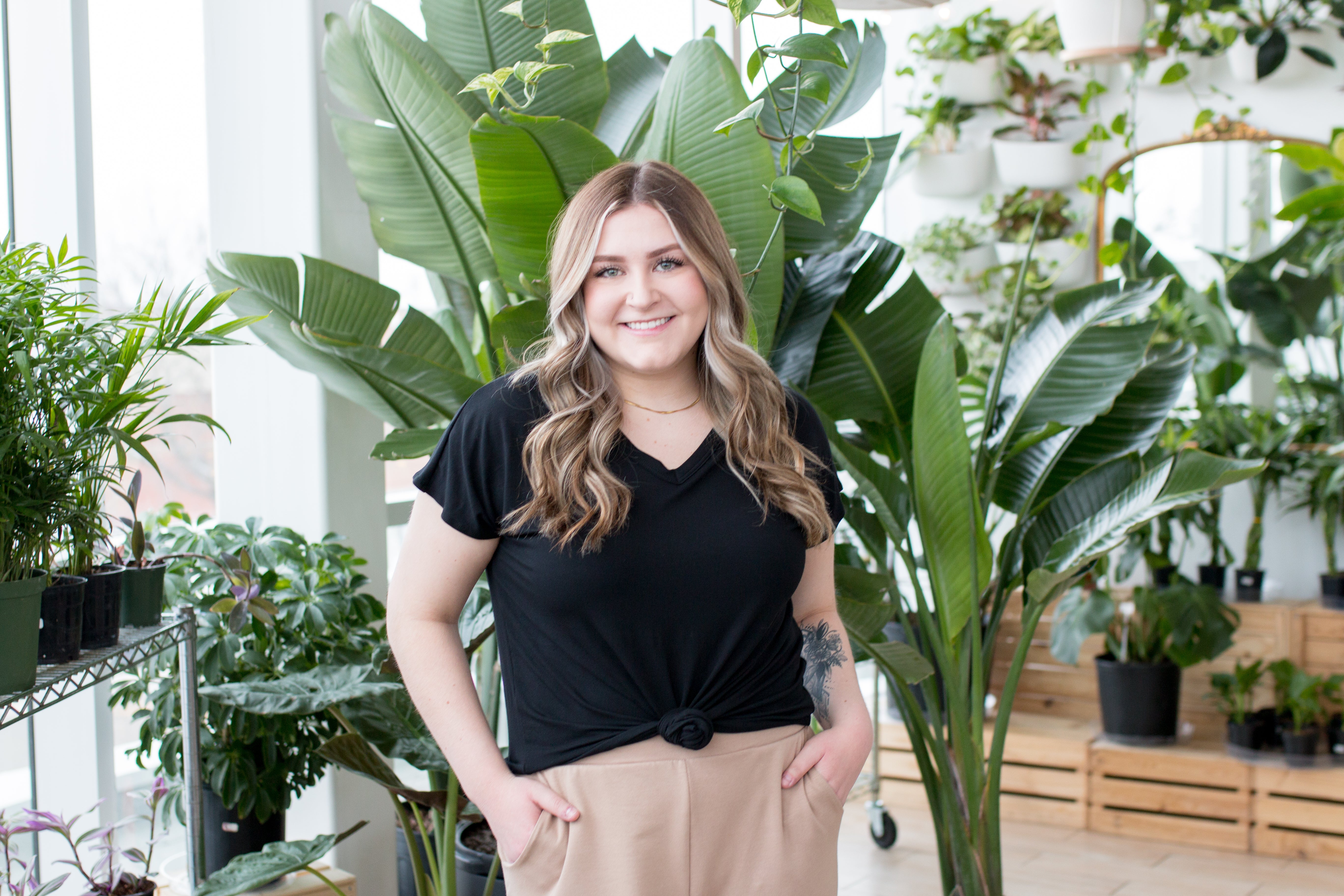 blonde woman standing in black vneck t shirt in front of plant