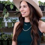 close up of a woman wearing a tan hat and a green dress with a silver necklace