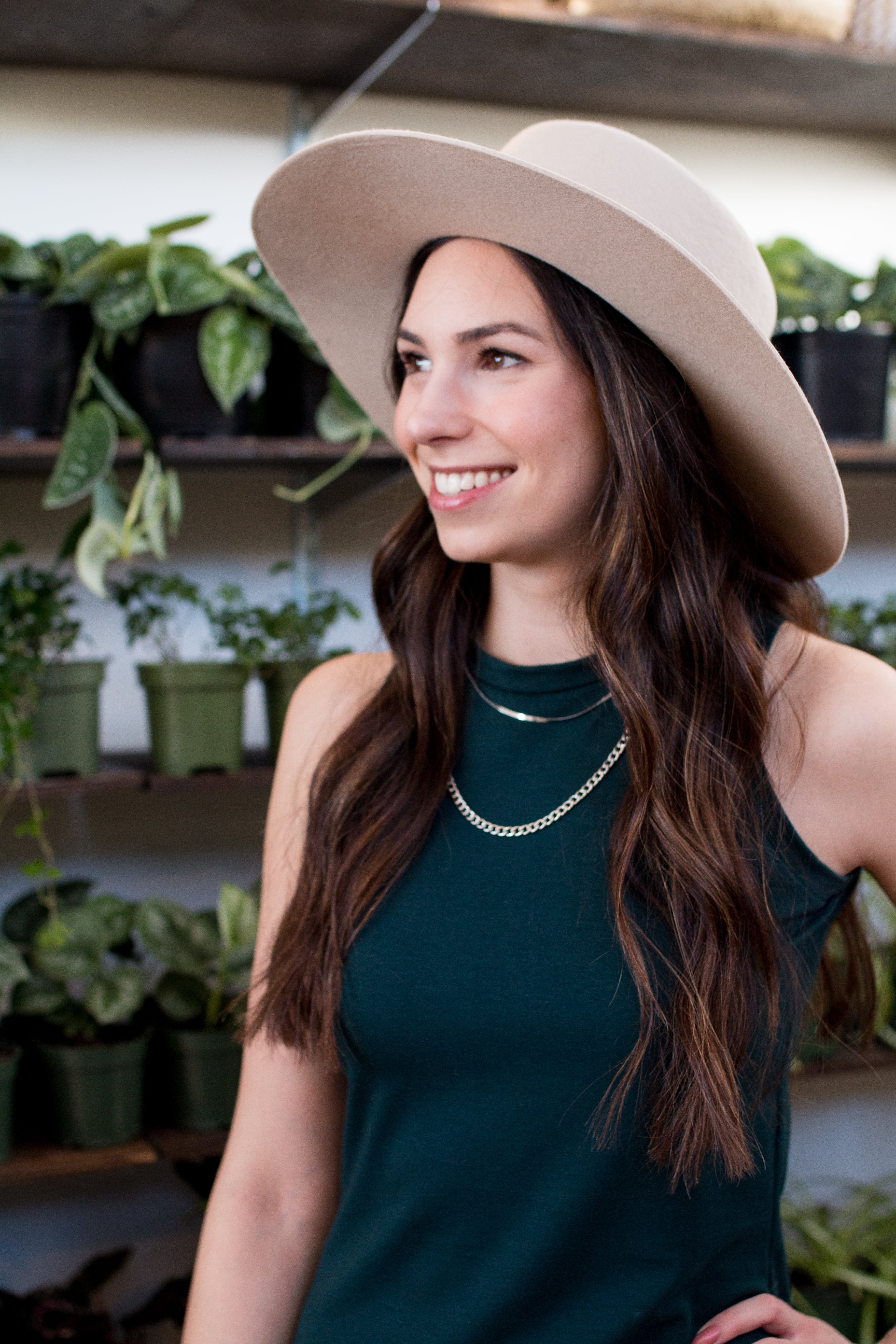 close up of a woman wearing a tan hat and a green dress with a silver necklace