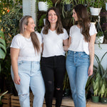 three women standing smiling alll wearing the same white v-neck t-shirt for women in bamboo with jeans