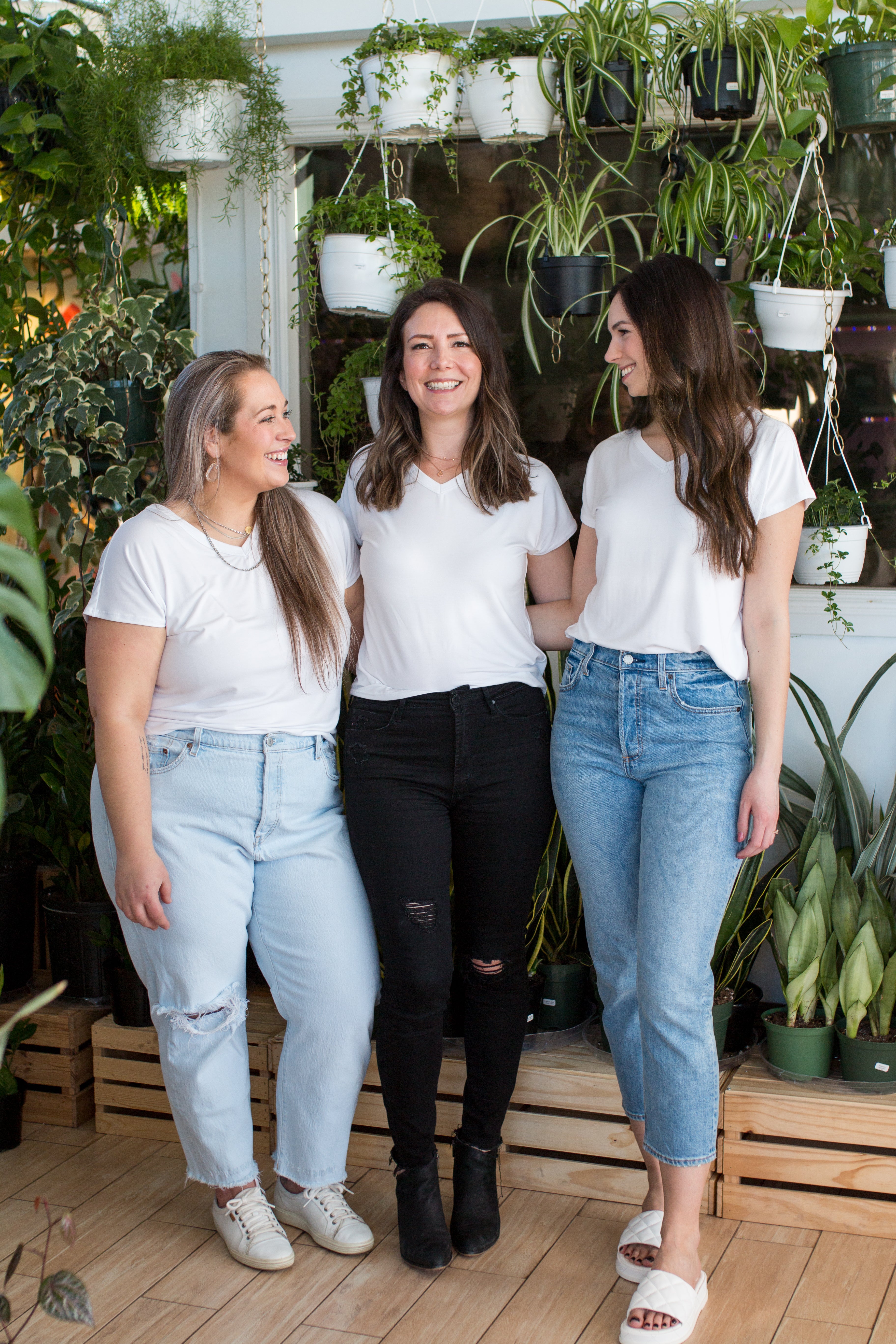 three women standing smiling alll wearing the same white v-neck t-shirt for women in bamboo with jeans