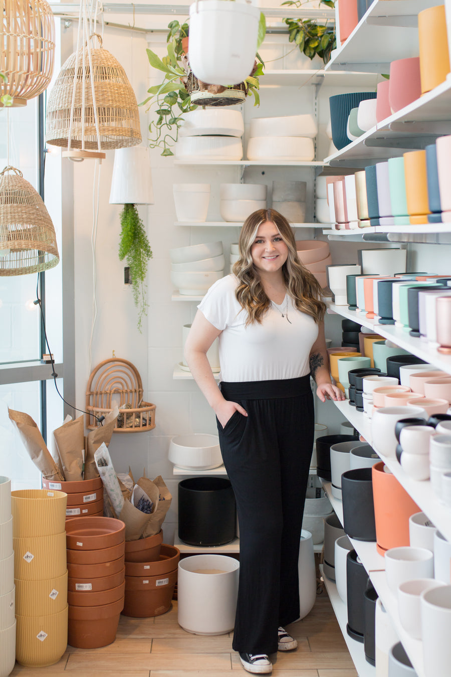 woman wearing a white vneck tshirt and black wide leg pants standing in a room with plant pots