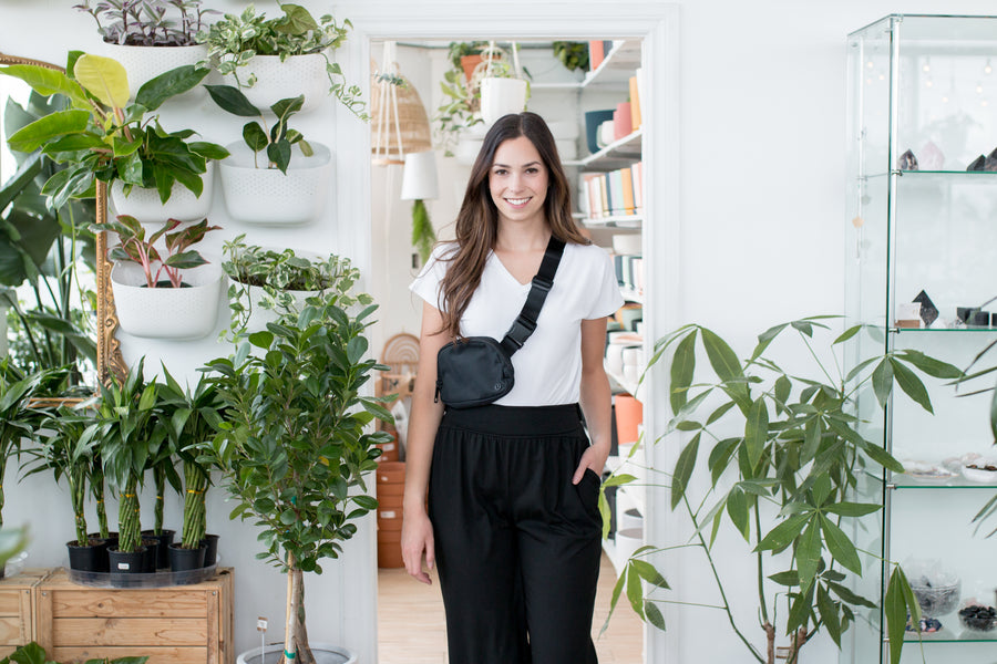 woman wearing a white vneck tshirt and black wide leg pants standing in front of a door with her hand in her pocket with a fanny pack 